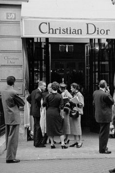 a group of people standing in front of a christian dior store on a city street