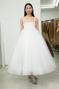 a woman standing in front of a white wall wearing a dress with spaghetti straps and a tulle skirt