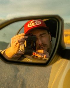 a man taking a selfie in the side mirror of a car with his camera