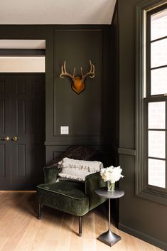 a living room with a green chair and deer head on the wall