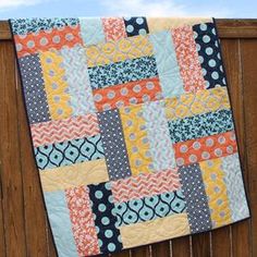 a quilt hanging on the side of a wooden fence with blue sky and clouds in the background