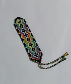 a multicolored beaded tie is hanging on a white wall with a black cord