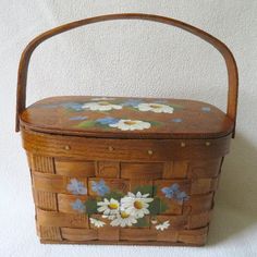 a wooden basket with flowers painted on the side and handles, sitting against a white wall