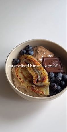 a bowl filled with bananas and blueberries next to a bar of chocolate on the side