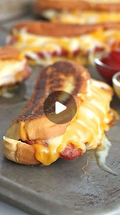 hotdogs with cheese and ketchup on a baking sheet next to condiments