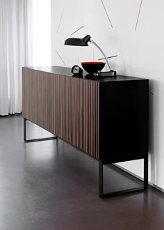 a black and wooden cabinet with a lamp on top next to it in front of a white wall