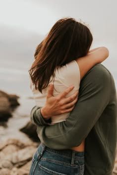 a man and woman hugging on the beach next to the ocean with their arms around each other