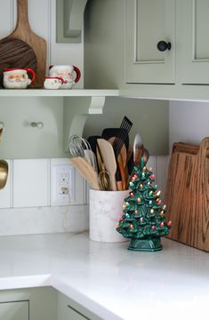 a small christmas tree sits on the kitchen counter next to cutting boards and utensils