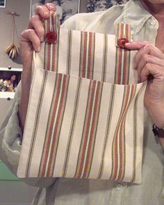 an older woman holding up a piece of fabric with red buttons on it and two hands