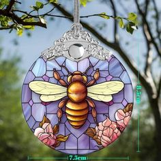 a stained glass bee ornament hanging on a tree branch with pink flowers and leaves