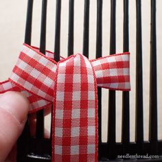 a hand holding a red and white striped ribbon on top of a black bird cage