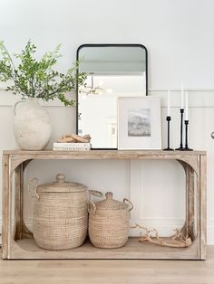 a wooden table with baskets on top and a mirror above it next to a plant