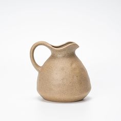 a brown ceramic pitcher sitting on top of a white table next to a black object