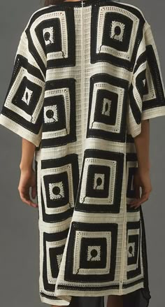 a woman is wearing a black and white crocheted coat with squares on it