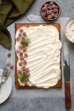 a cake with white frosting and berries on it next to other desserts, forks and knives