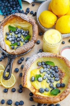 two lemon pies with blueberries and powdered sugar on the top, surrounded by fresh fruit