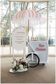 an ice cream stand with pink and white flowers on the ground next to a bicycle