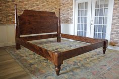 a wooden bed frame sitting on top of a rug in a room with brick walls