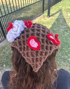 a woman wearing a crocheted hat with flowers on it's top and two hearts in the middle