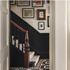 an entry way with stairs and framed pictures on the wall above it, along with a black stair case