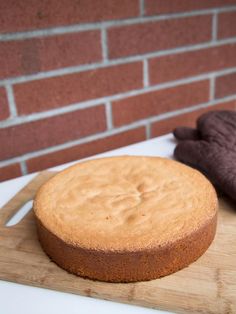 a round cake sitting on top of a wooden cutting board next to a brick wall