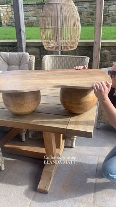 a woman sitting on the ground next to a wooden table with two large bowls on it