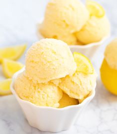 two bowls filled with lemon ice cream next to sliced lemons on a marble surface