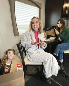 a woman sitting in a chair with a cardboard box on her lap next to another woman holding a cup