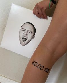 a person with a tattoo on their arm holding a piece of paper that has a drawing of a man's face