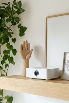 a white projector sitting on top of a wooden shelf next to a potted plant