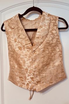 Step back in time with this exquisite piece of Victorian history--a gentleman's wedding waistcoat, dating back to 1855. This hand-stitched vest was crafted with meticulous attention to detail, featuring a luxurious cream silk brocade front and a durable linen/cotton back. The waistcoat is adorned with five fabric-covered buttons and a rounded collar, epitomizing the elegance and refinement of the Victorian era. Key Features: * Material: Warm golden-cream silk brocade front, linen/cotton back * Details: Five fabric-covered buttons, rounded collar * Fit: Adjustable back with two fabric tabs, three metal eyelets per side, and lacing for a perfect fit * Size: Chest 27", Length 19" (Smallish size) * Provenance: Handwritten tag indicates this waistcoat was worn at Grandpa Price's wedding in 1855 Fitted Gold Vest Elegant Style, Fitted Gold Elegant Vest, Elegant Silk Vest For Formal Occasions, Gold Fitted Vest, Elegant Gold Fitted Vest, Fitted Sleeveless Vest For Wedding, Classic Fitted Nehru Jacket For Wedding, Classic Sleeveless Three-piece Suit For Wedding, Elegant Fitted Silk Vest