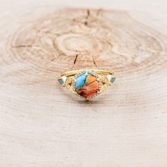 a gold ring with an orange and blue stone in the center on a wooden surface