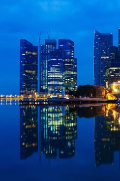 the city skyline is lit up at night and reflecting in the water with its lights on