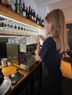 a woman standing in front of a counter filled with wine glasses and cups next to an espresso machine