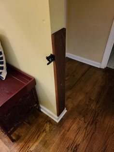 the corner of a room with a bench and wooden floor next to a door that has a black handle on it