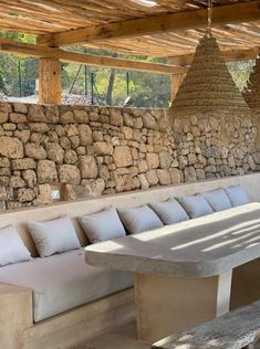 an outdoor seating area with stone walls and hanging baskets on the ceiling, along with white cushions