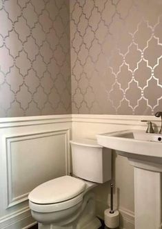 a white toilet sitting next to a sink in a bathroom under a wallpapered pattern