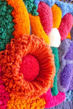 colorful crocheted items are arranged in rows on the table, with one large flower at the center