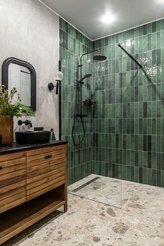 a bathroom with green tiles on the wall and wooden cabinet in the middle, along with a black sink