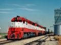 a red and white train traveling past a grain silo