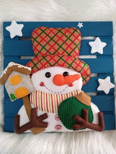 a snowman with a hat and scarf is sitting on a blue wooden plank, holding a piece of bread