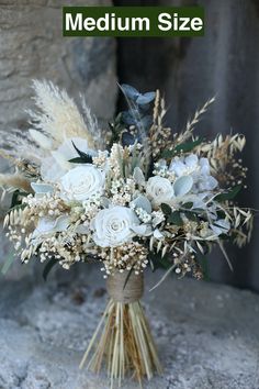 a bridal bouquet with white flowers and greenery on a stone surface in front of a rock wall