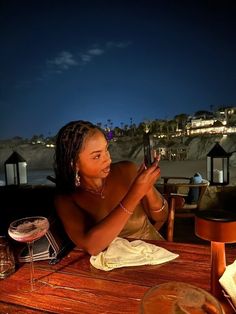 a woman sitting at a table with a cell phone in her hand and looking at the screen