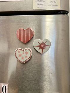 three heart shaped magnets sitting on top of a stainless steel refrigerator freezer door