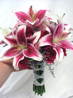 a bridal bouquet with pink lilies and red roses in someone's hand