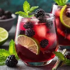 two glasses filled with blackberry lemonade and mint garnish on top of a table