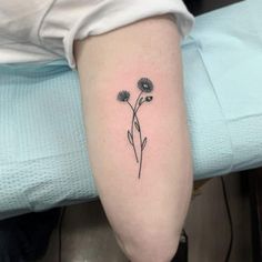 a small flower tattoo on the right arm and leg, with three petals in black ink