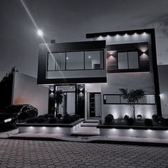 a black and white photo of a modern house at night with lights on the windows