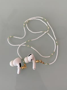 two ear buds are attached to a white beaded necklace on a gray surface with gold accents