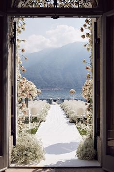 an open door leading to a wedding ceremony with white chairs and flowers on the aisle